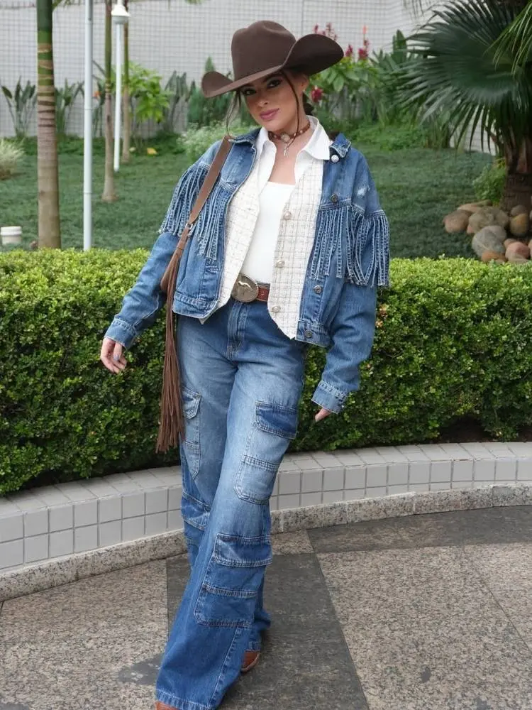 Mulher de pele clara com camisa branca, colete xadrez, jaqueta jeans com franjas e calça jeans 