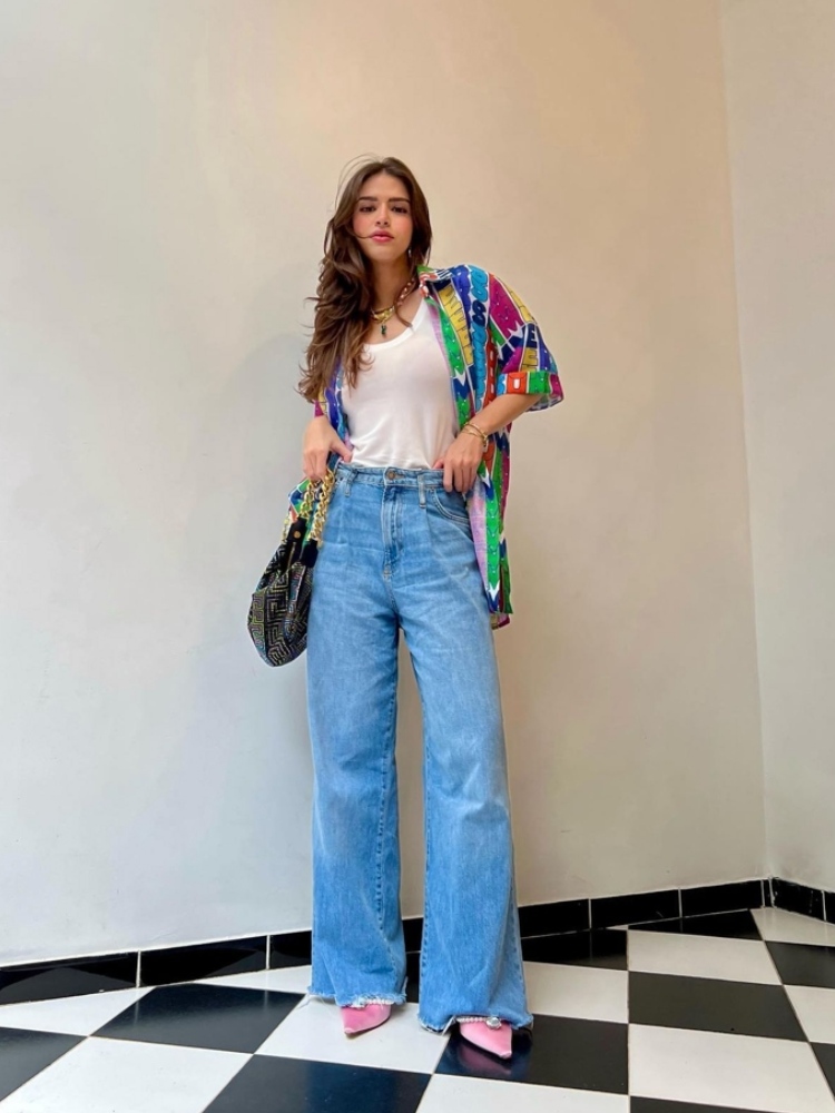 mulher usando regata branca com sobreposição com camisa colorida, calça jeans wide leg, bolsa de corrente e sapato rosa tipo scarpin