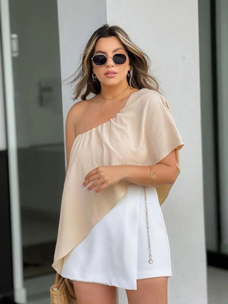 mulher usando roupa de ano novo na praia com blusa assimétrica, short saia branco e cinto dourado