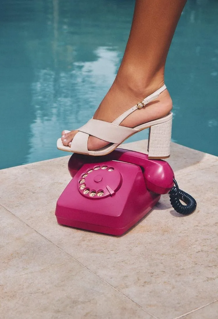 Pé de modelo usando sandália de salto bloco branca e pisando em telefone rosa