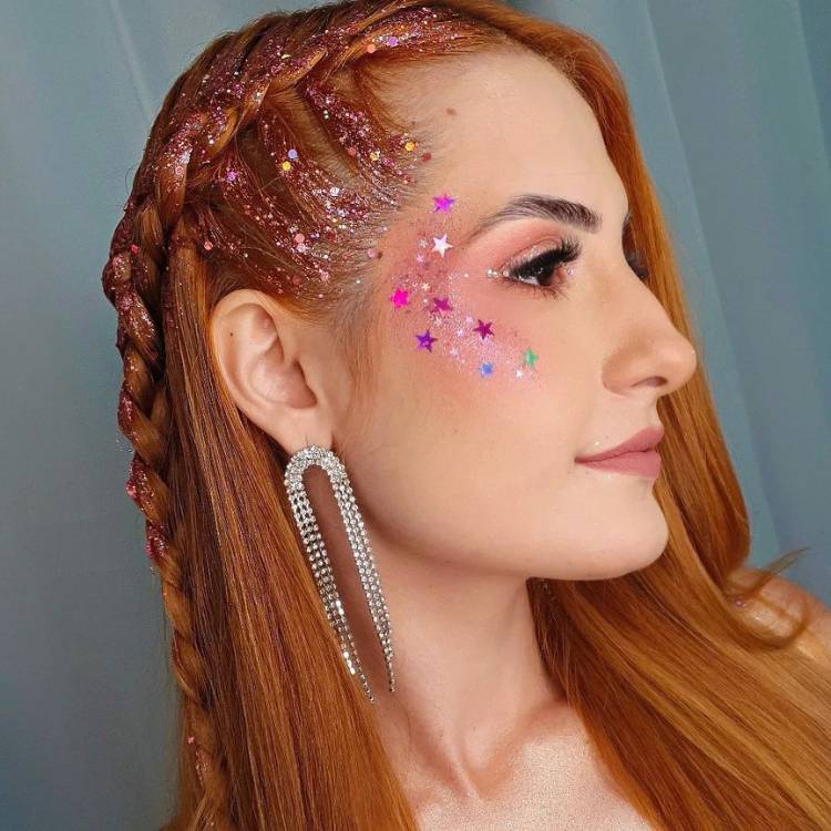 Mulher ruiva de pele clara com make nude nos olhos e estrelas coloridas no rosto. 