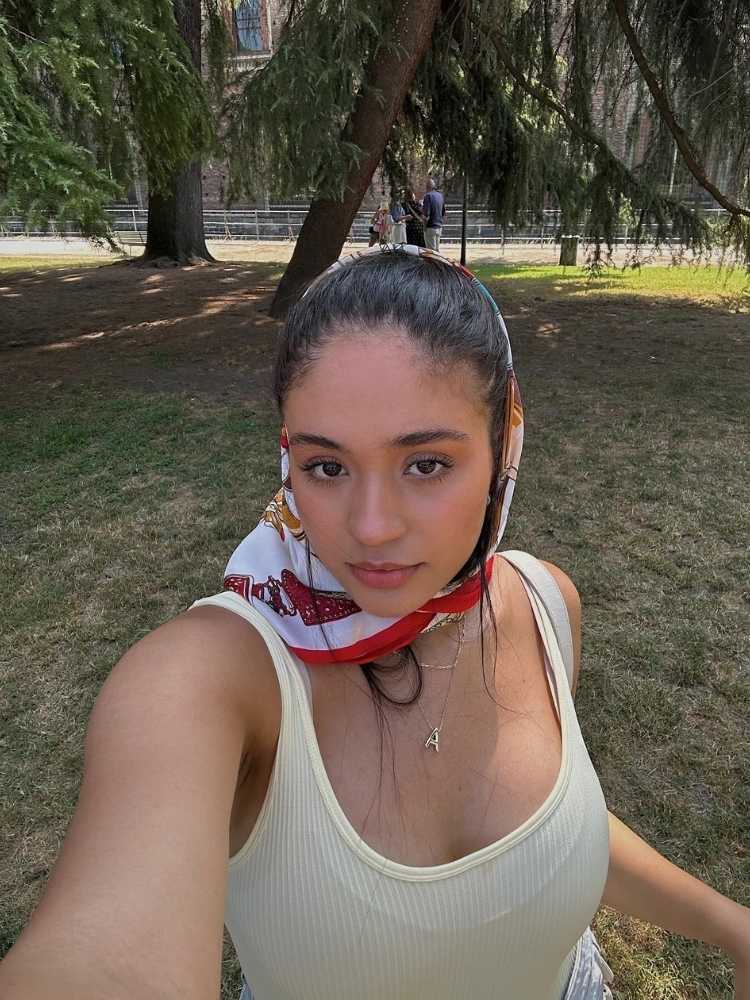 Bia Araújo em jardim usando regata branca e lenço na cabeça 