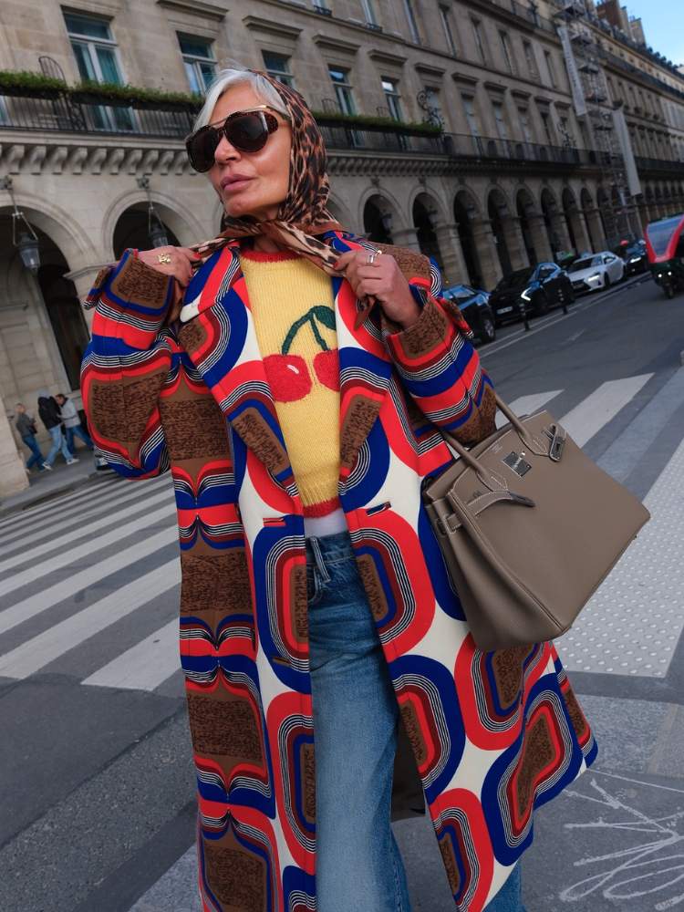 Grece usando lenço animal print ma cabeça, suéter amarelo com desenho de cereja, sobretudo colorido e calça jeans 