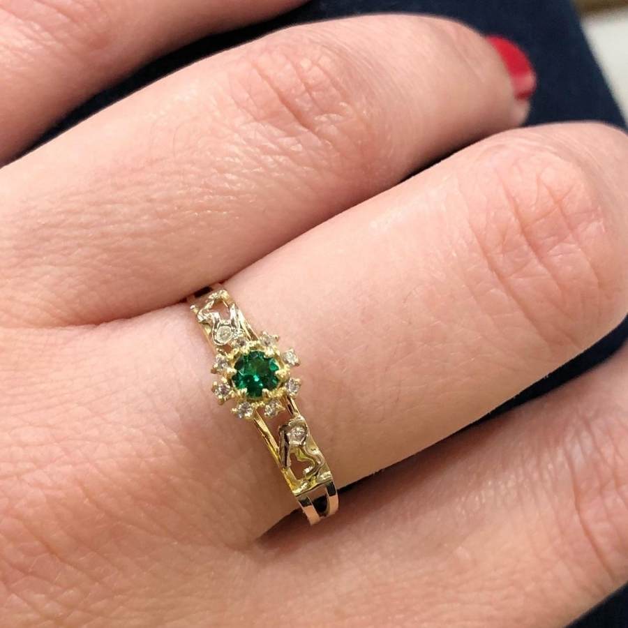 Pessoa de pele clara usando anel dourado com pedra verde no dedo médio
