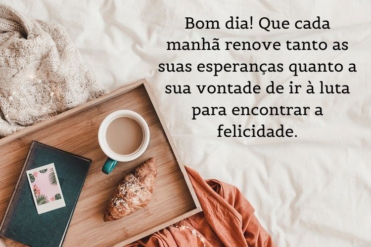 Foto de cama com bandeja de madeira com livro, café e croissant e frase: Bom dia! Que cada manhã renove tanto as suas esperanças quanto a sua vontade de ir à luta para encontrar a felicidade.