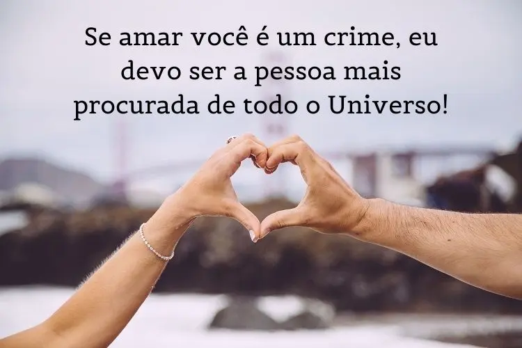 Foto de duas pessoas de pele clara fazendo coração com as mãos e frase "Se amar você é um crime, eu devo ser a pessoa mais procurada de todo o Universo!"