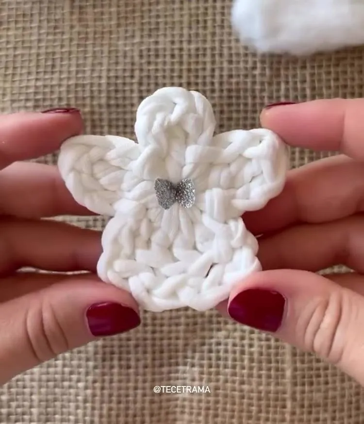 Mãos com unhas vermelhas segurando Anjo de crochê de Natal branco com laço prateado