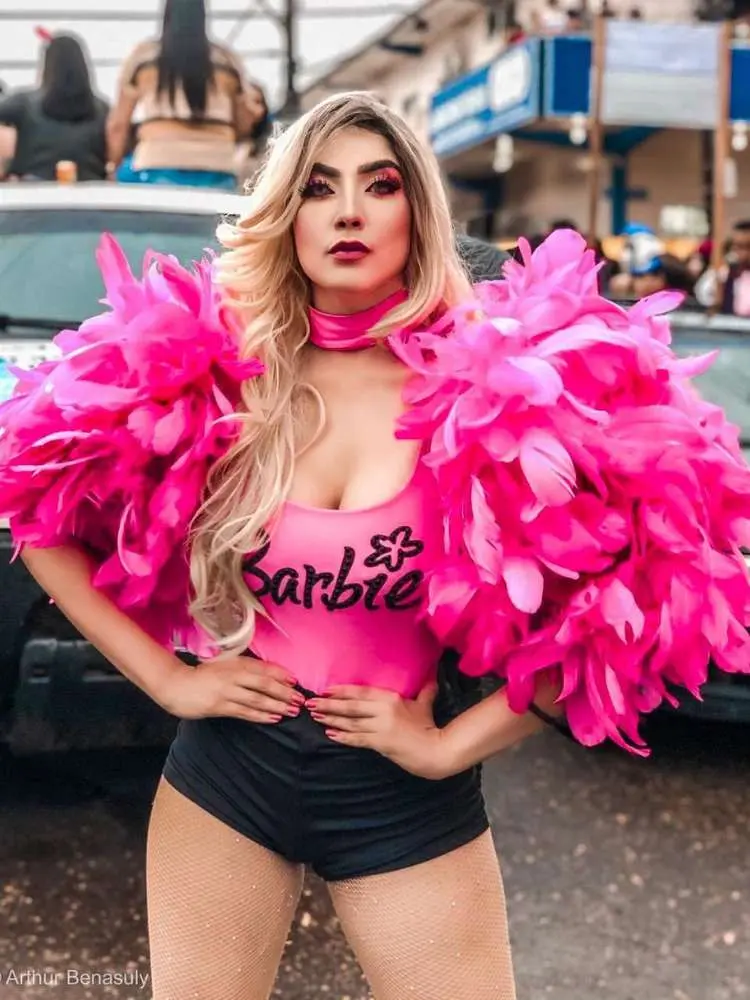 Mulher de pele clara com body da Barbie, ombreira de penas e hot pant preta