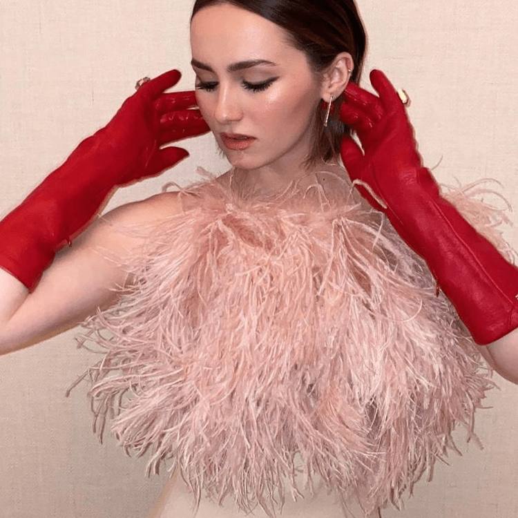Maude Apatow usando luvas vermelhas e top de penas rosa