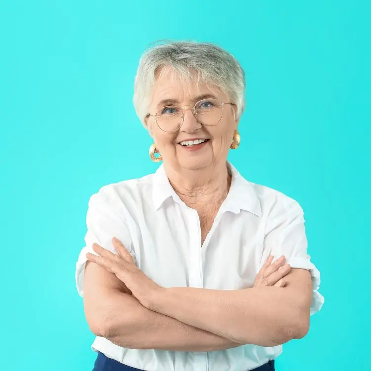 Senhora de cabelo curto usando blusa branca, sorrindo de braços cruzados em fundo verde água