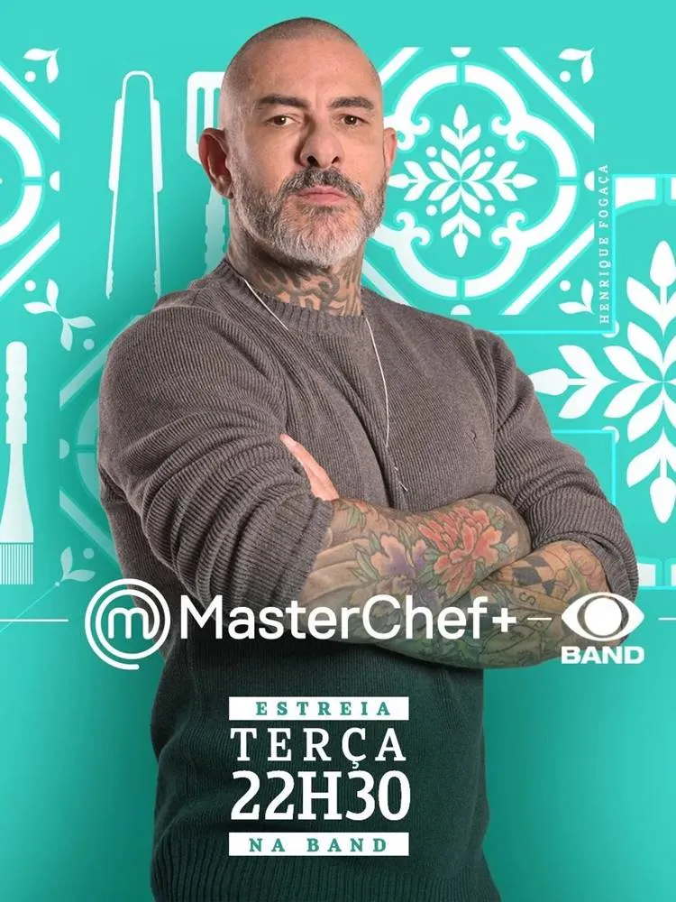 Foto de Fogaça do MatserChef+ 2023 com suéter e de braços cruzados em fundo verde água com desenhos de cozinha branco