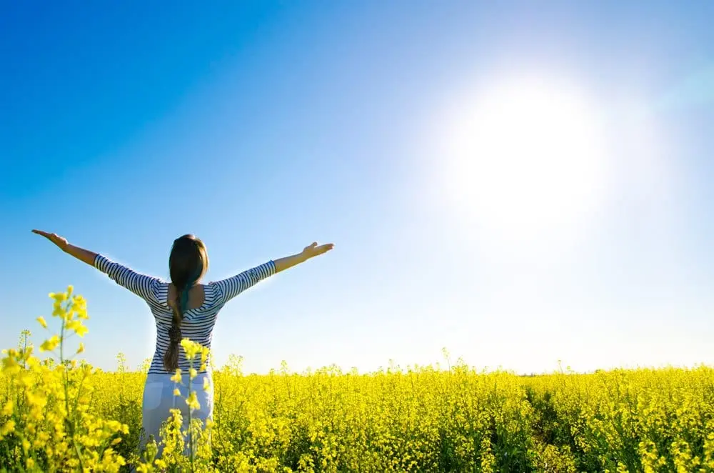 Foto de mulher em campo de flores amarelas com braços abertos para o sol