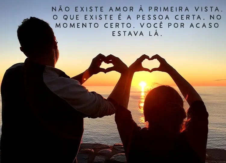 Homem e mulher de costas para a foto e de frente para o mar, fazendo coração com as mãos para o pôr do sol e frase "Não existe amor à primeira vista. O que existe é a pessoa certa. No momento certo. Você por acaso estava lá."