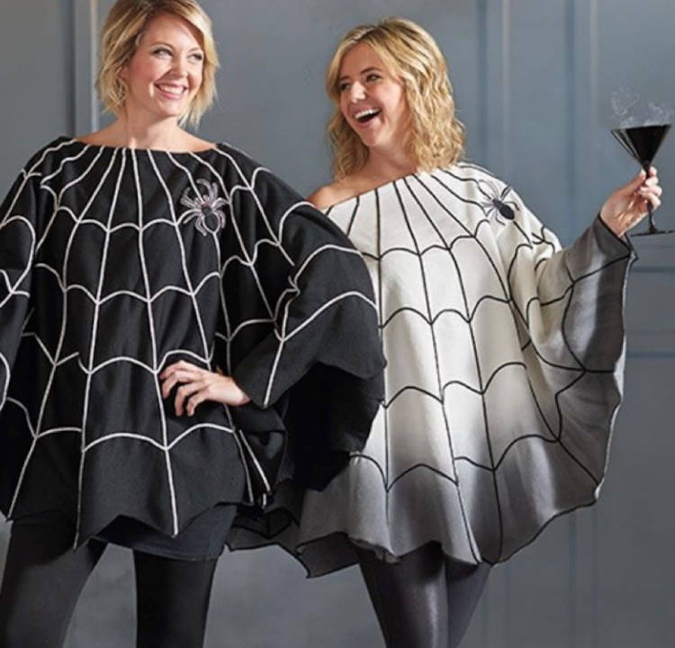 Duas mulheres loiras de pele clara usando poncho de teia de aranha, uma delas usando um preto e outra usando um branco 