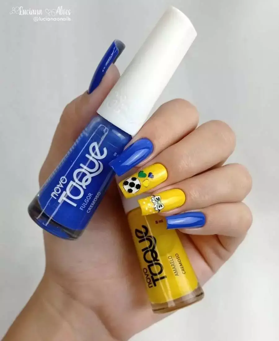 Imagem de mão com unhas decoradas.  Cores usadas, verde, amarelo, azul e branco. Polegar: azul. Indicador: azul. Dedo Médio, amareo com adesivos de corações e bola de futebol. Anelar: amarelo com adesivo de Minnie. Mínimo: azul.