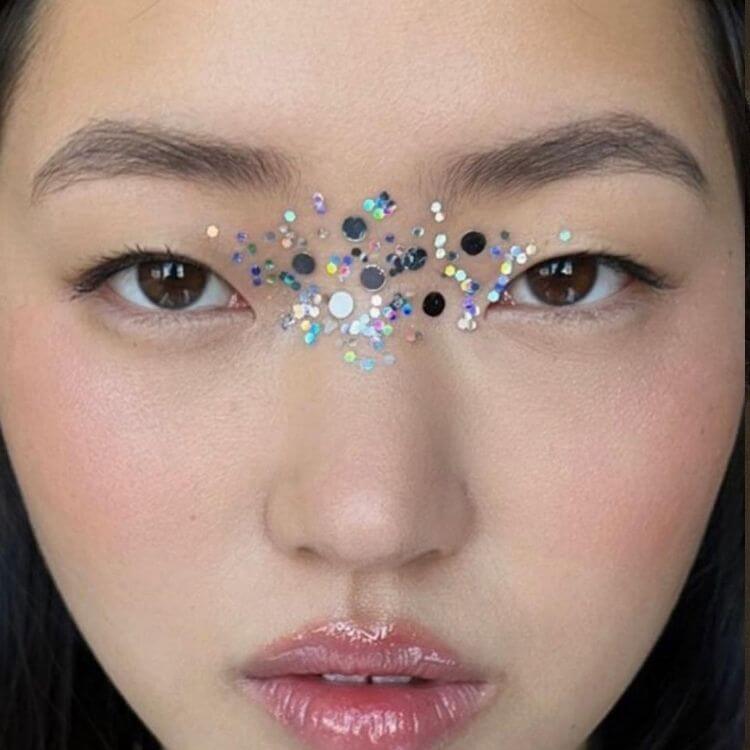 Mulher de origem asiática com glitter flocado no nariz, entre os olhos
