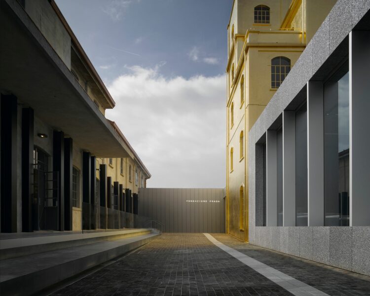 Fundação Prada, Milão, Miuccia Prada, moda e arte Foto mostra o corredor de entrada da Fundação Prada com edifícios em tom de prateado e dourado