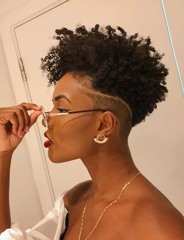Mulher negra com cabelo crespo, make delineado e batom vermelho, usando joias douradas, óculos e roupa branca