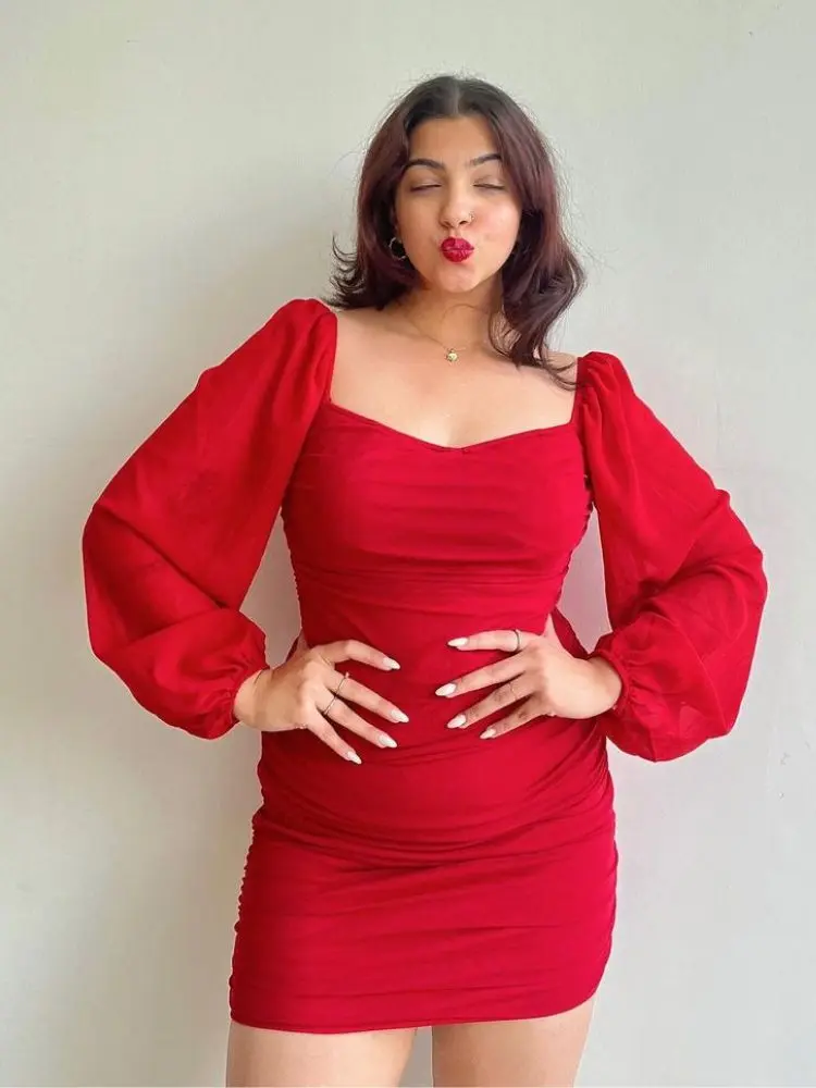 Mulher com as mãos na cintura usando vestido vermelho de mangas bufantes para o Natal