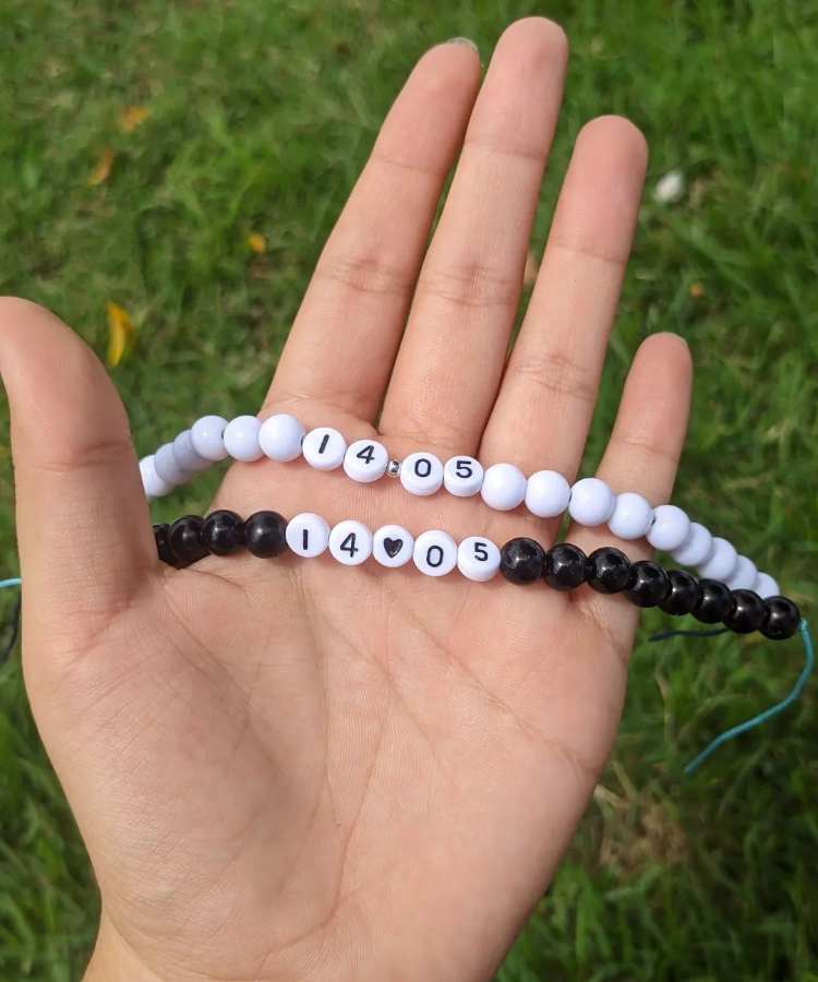 Mão segurando pulseiras de miçangas preta e branca com data especial para casal
