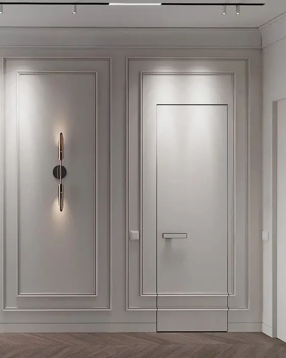 Parede clara com luminária e boiserie disfarçando porta "invisível"