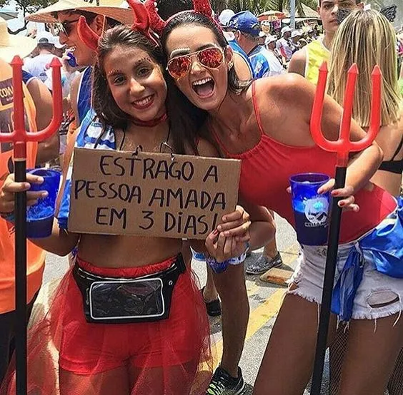 Foto de duas mulheres fantasiadas de diabo e uma usa placa "estrago a pessoa amada em 3 dias"