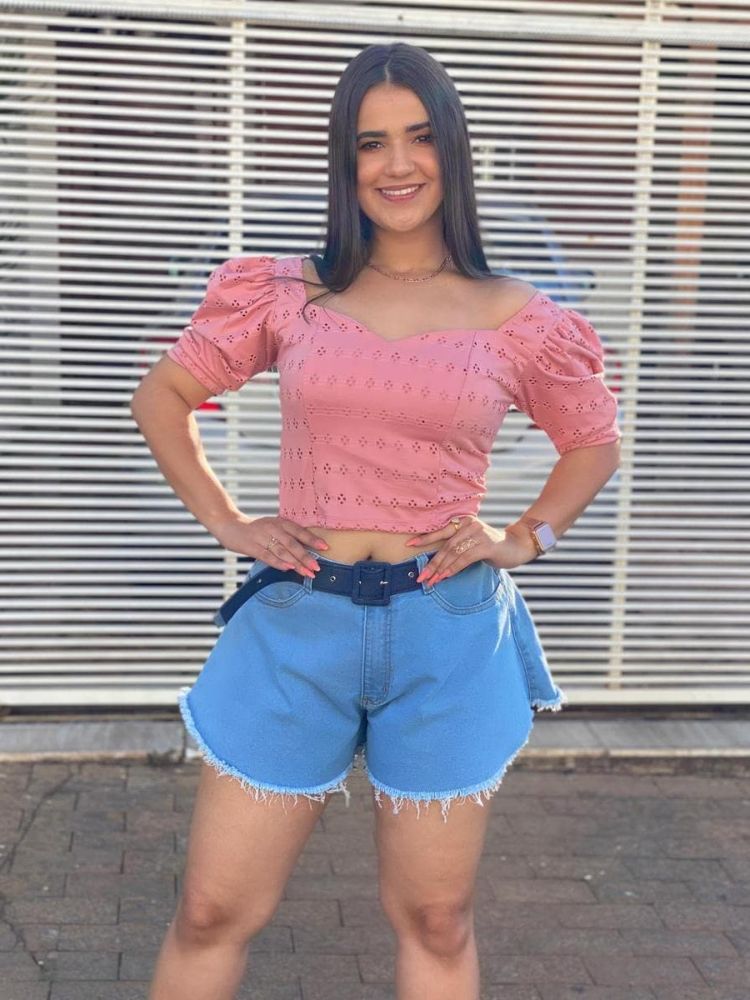 Mulher de pele morena usando shorts jeans godê com cinto preto e cropped rosa
