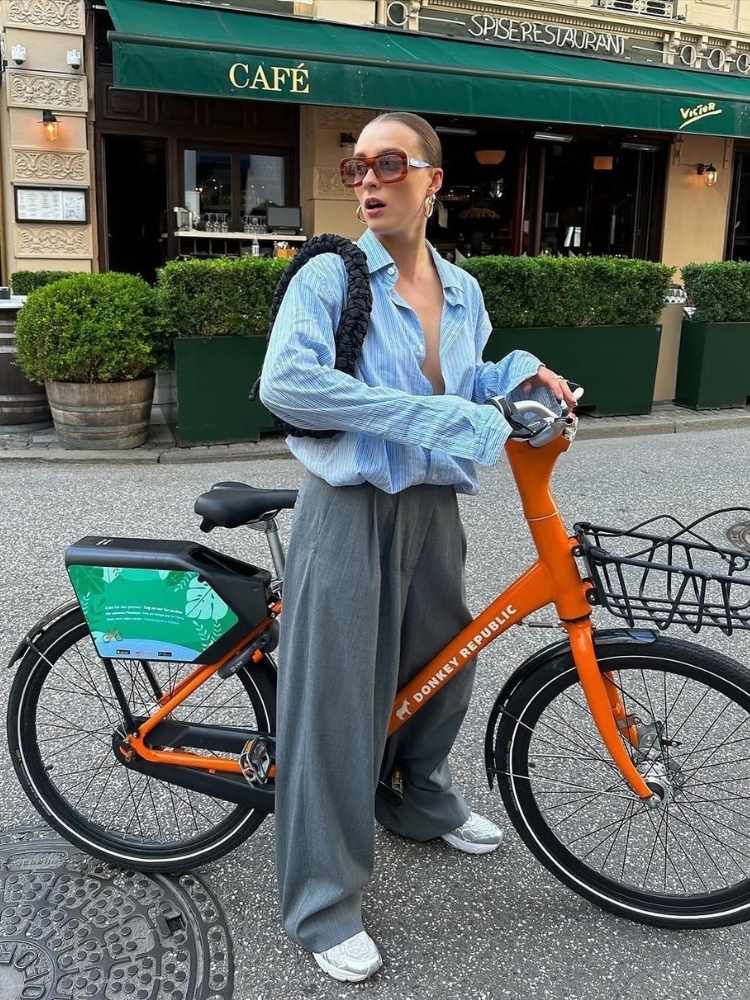 Mulher de pele clara usando camisa social auzl, calça de alfaiataria cinza e óculos de sol oversized