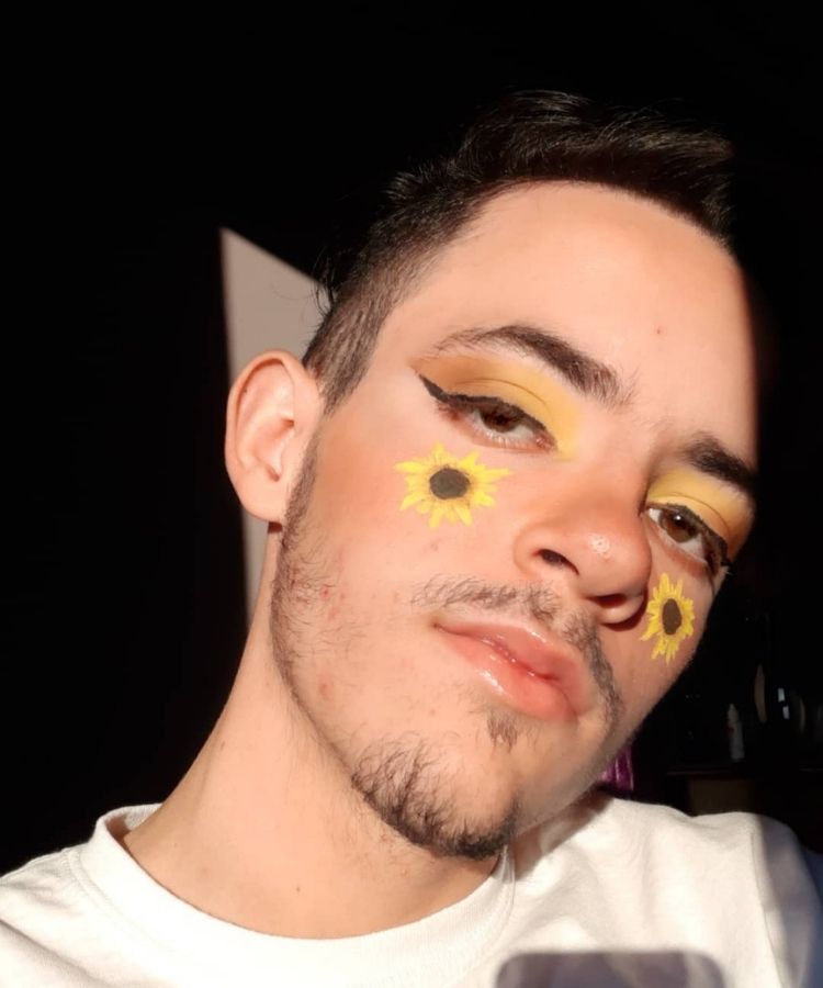 Homem de pele clara usando maquiagem amarela e girassóis na bochecha