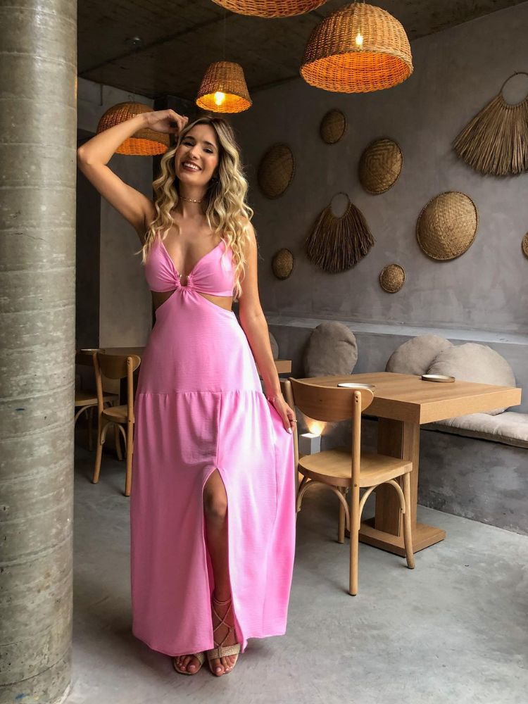 Mulher loira de pele clara usando vestido rosa em espaço decorado com conchas, além de cabelos soltos
