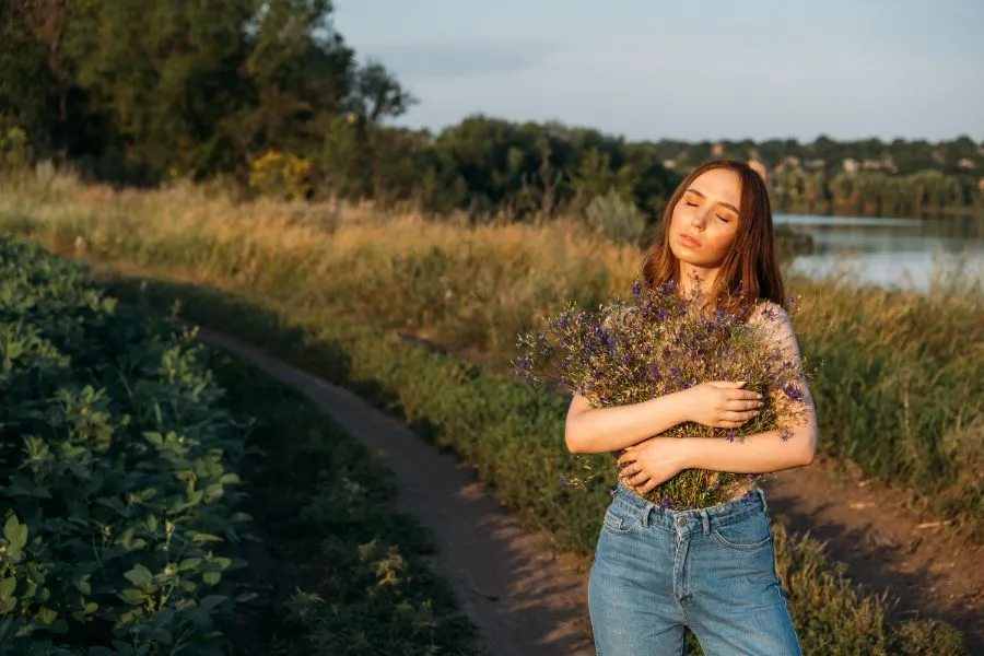 mulher usando calça jeans e abraçando buquê de flores do campo, autoestima