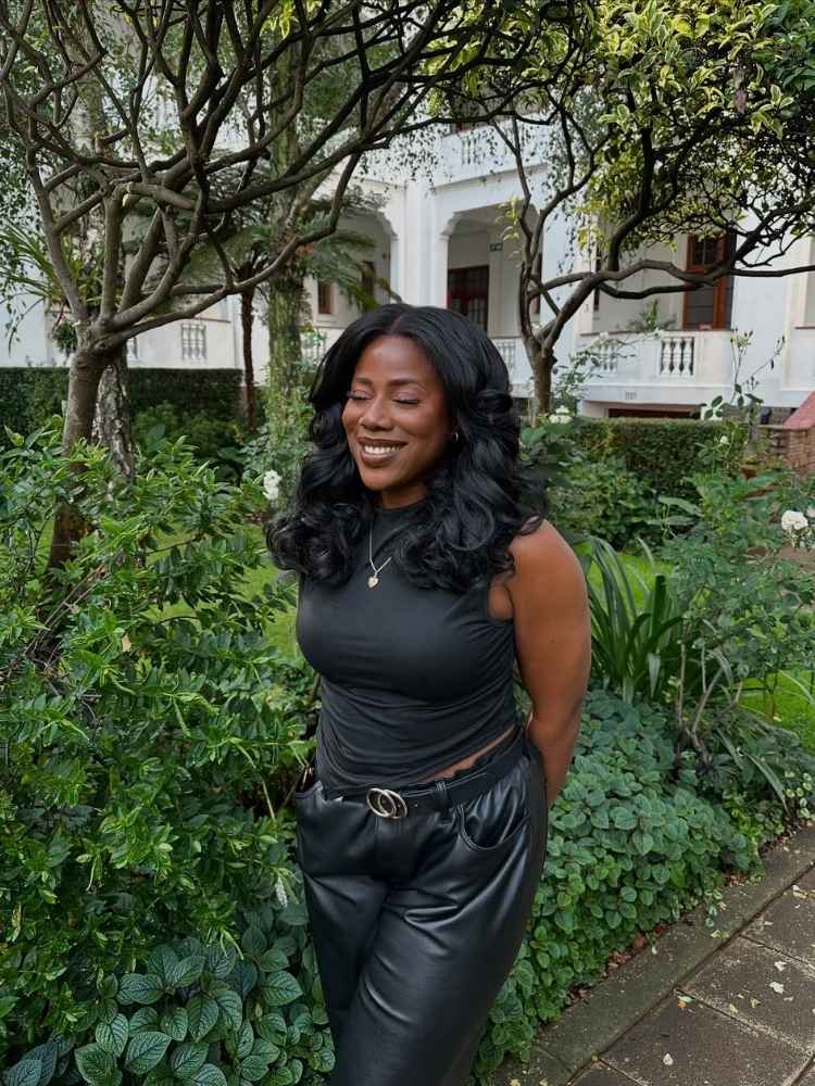 Mulher de pele negra com look preto e cabelos em ondas volumosas 