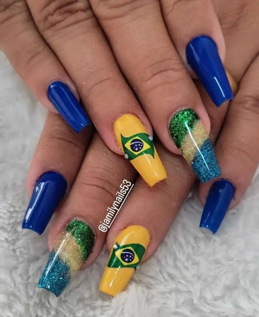 Imagem de mão decoradas com esmalte.  Cores usadas, verde, amarelo, azul e branco. Indicador: azul. Dedo Médio, glitter verde, dourado e azul. Anelar: amarelo com bandeira em adesivo + pedinhas decorativas. Mínimo: azul.