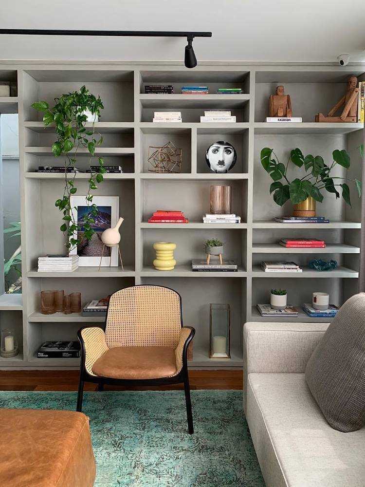 Estante em cinza com pratos de porcelana com rostos pintados, diversos vasos de planta, quadros e outros itens decorativos. 
