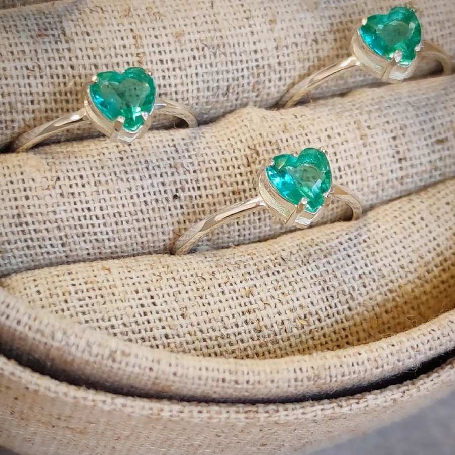 Três anéis dourados com pedras verdes em formato de coração