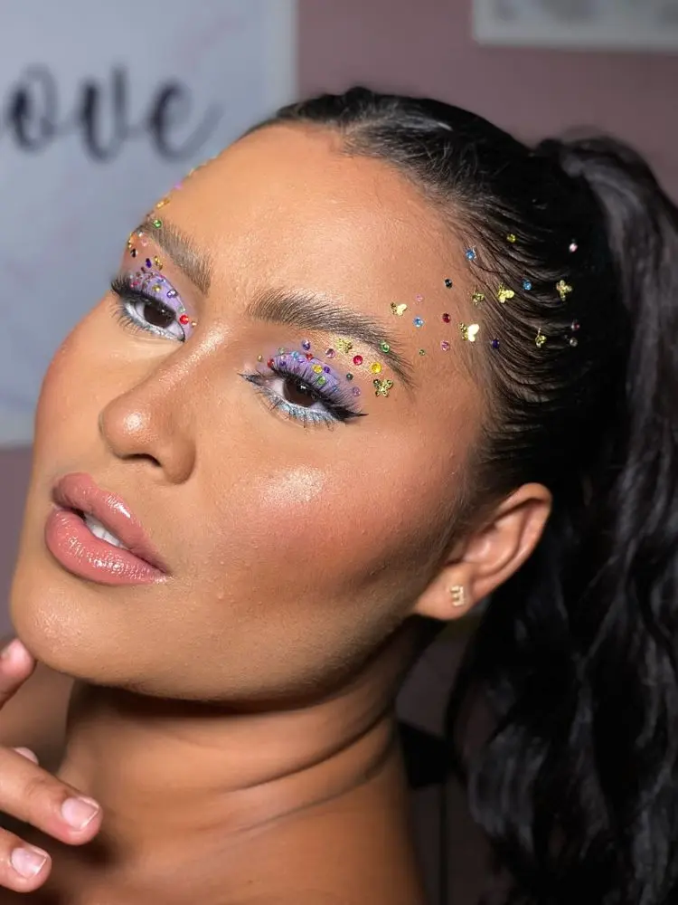 Mulher de pele morena com sombra roxa e strass em diferentes formatos, desde o olho até o cabelo