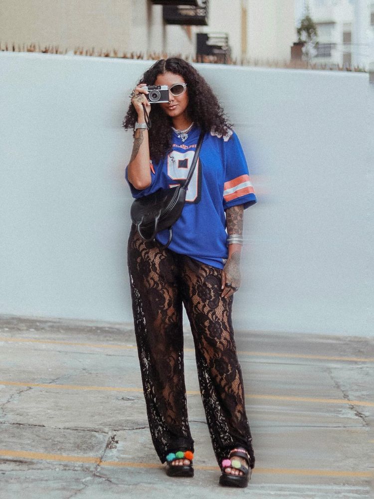 Mulher de pele negra usando jearsey azul, calça de renda preta e acessórios 