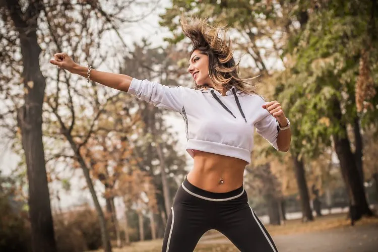Mulher com roupa de exercitar dançando ao ar livre em jardim com várias árvores