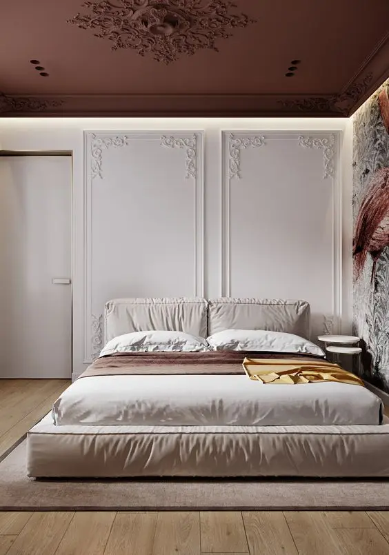 Quarto de casal com quadro colorido à direita, cama, mesas ao lado da cama, parede branca com moldura trabalhada e teto marrom com moldura trabalhada