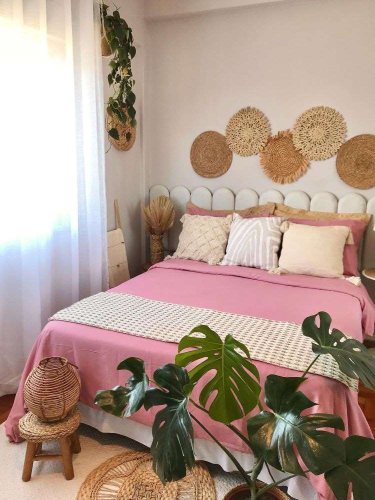 Quarto com cama de casal, itens decorativos redondos na parede, costela-de-adão no chão e vaso pendente com jiboia.