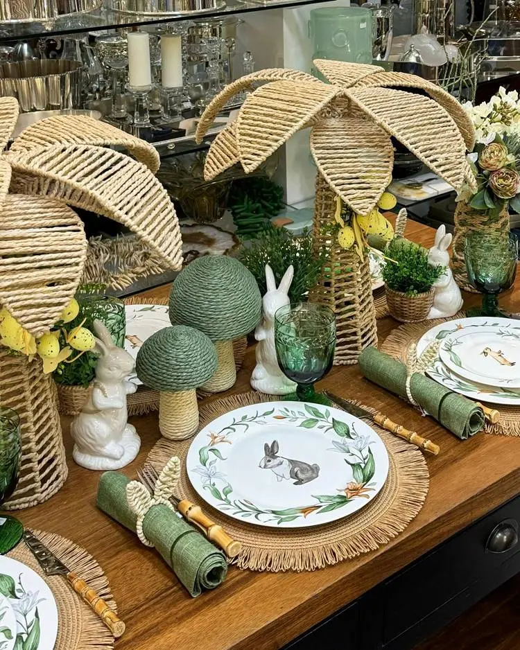  mesa posta para almoço de Páscoa chique com itens Verde trabalhados em palha e pratos com pinturas de coelho
