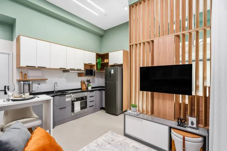 Integração de cozinha em verde, branco e cinza com sala com painel de madeira