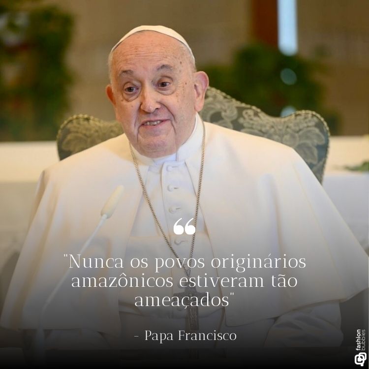 O Papa Francisco aparece sorrindo levemente, vestido com seus paramentos brancos e sentado em uma cadeira. Abaixo de sua imagem, está a frase: "Nunca os povos originários amazônicos estiveram tão ameaçados", com fundo desfocado e detalhes suaves.