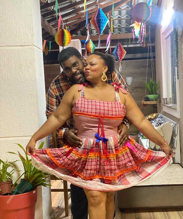 Casal com roupa de festa junina, ela de vestido tradicional e ele com camisa xadrez