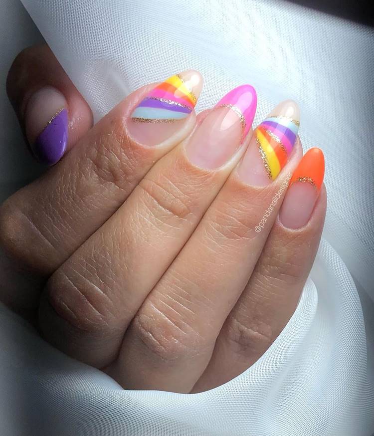 Mão com unhas arco-íris LGBTQIA+:  Polegar: natural com francesinha grossa lilás com risco dourado Indicador: arcoíris com riscos dourados Médio: cor natural da unha com francesinha rosa e risco dourado Anelar: arcoíris com riscos dourados Mínimo cor natural da unha com francesinha laranja e risco dourado