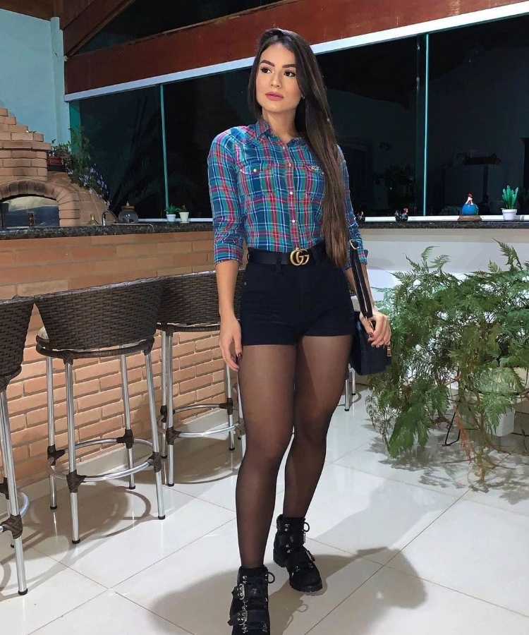 Menina com camisa xadrez, short preto, meia calça preta e bota preta