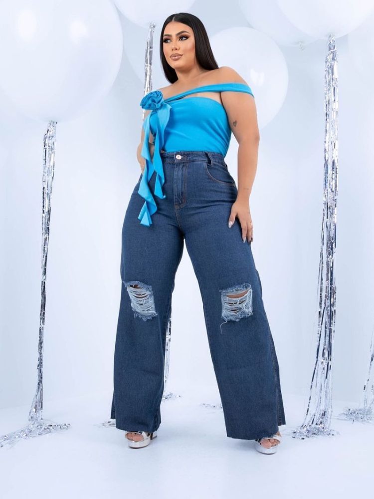Mulher de pele clara com cropped azul e calça jeans wide leg destroyed