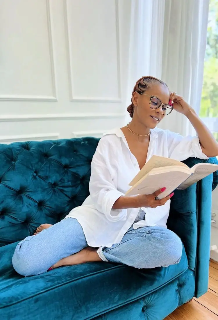 A cantora Aline Wirley do BBB 23 aparece sentada em um sofá com uma camisa branca lendo um livro