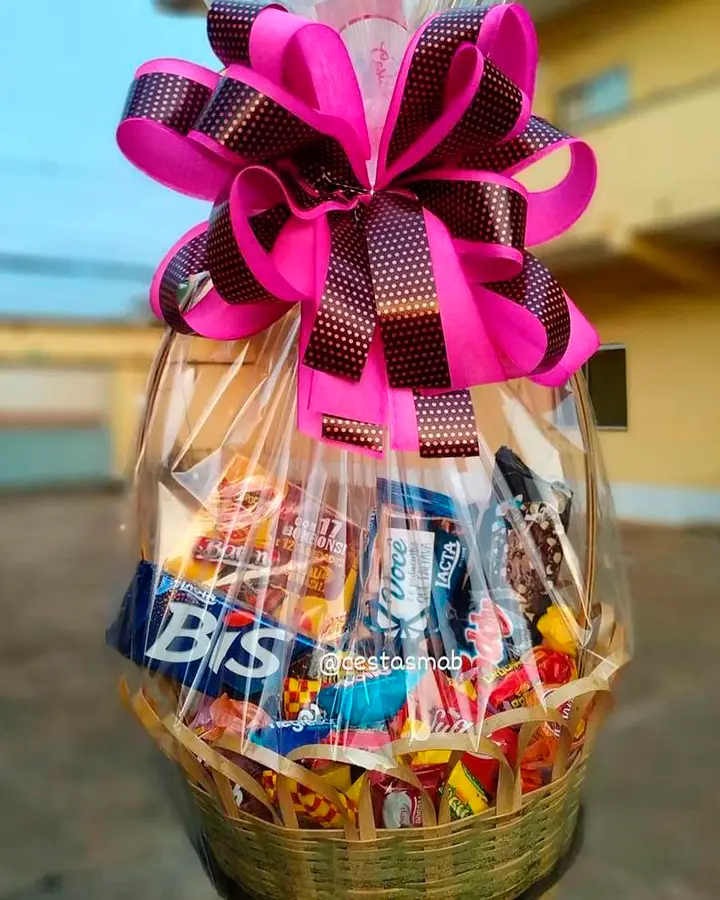 Cesta com vários doces dentro, decorada com um laço rosa