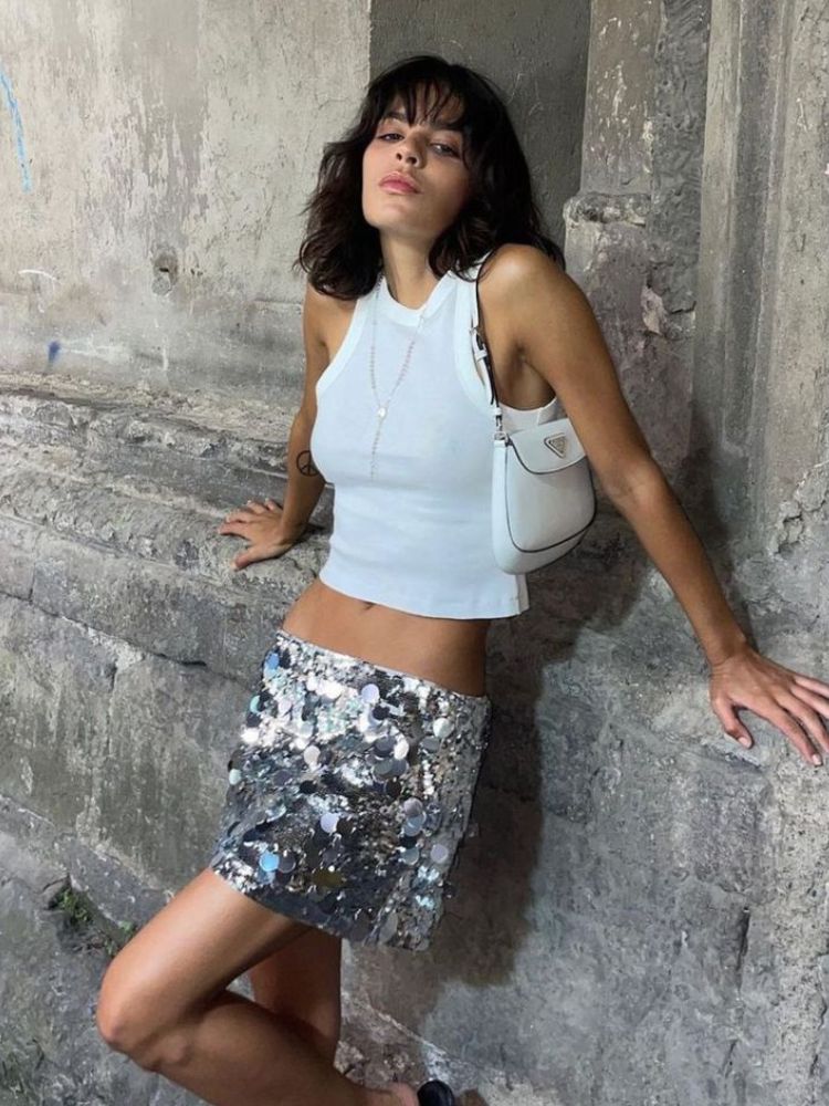 Mulher de pele clara com saia curta metalizada e cropped branco.